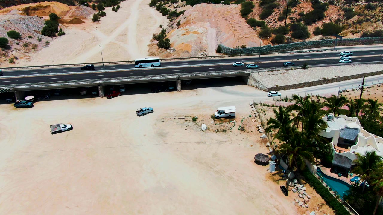 Aerial view in Punta Buzzards with traffic spread across the highway overpass, open sand below, rocky terrain above the road, and no visible people.