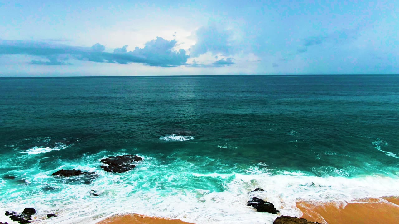 Aerial coastline view with foamy waves and scattered rocks.