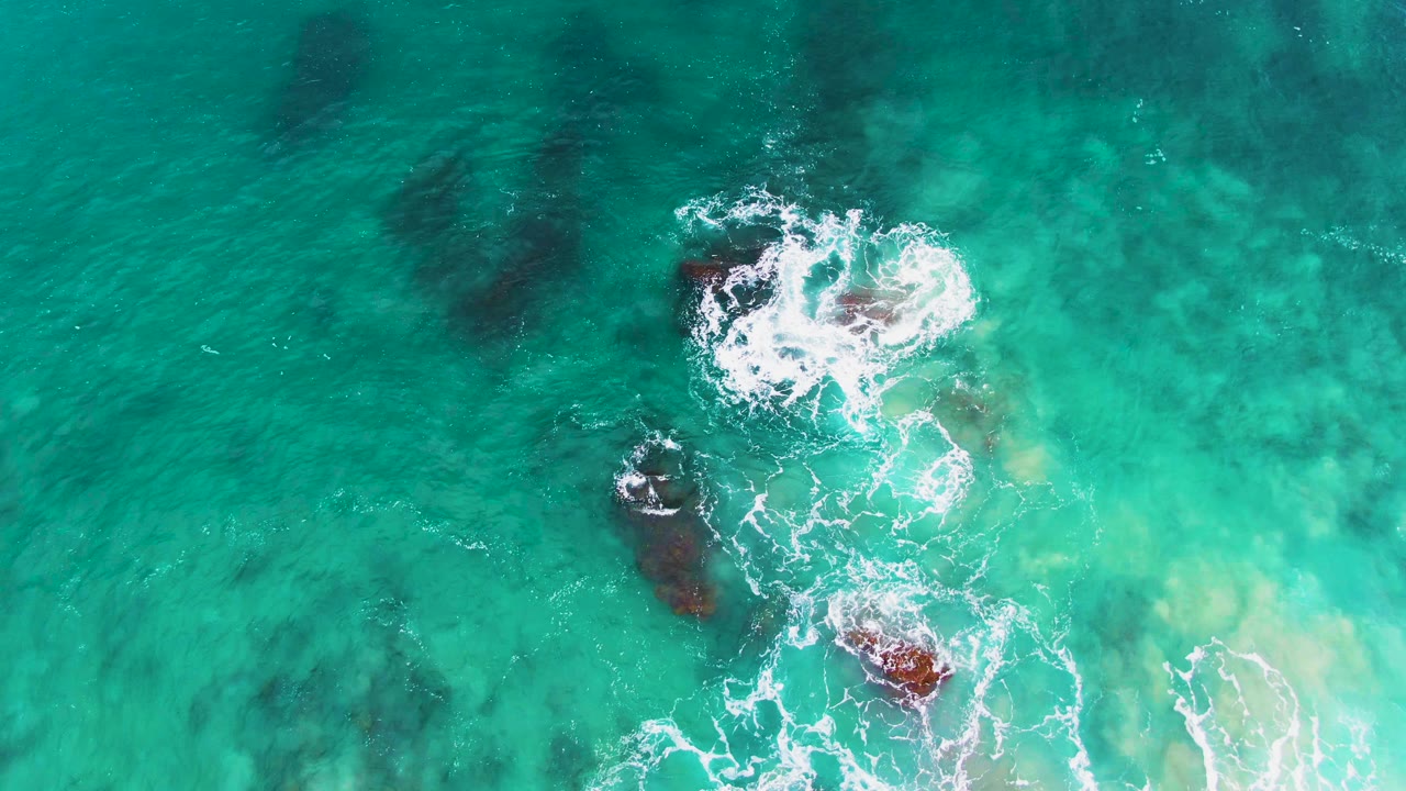 Foamy wave break over rocky seabed in shallow turquoise ocean