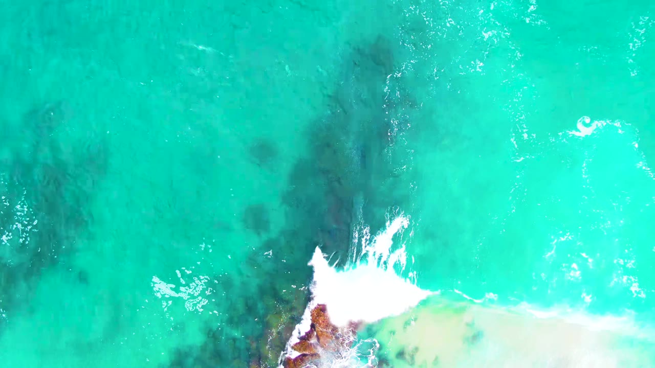 Overhead turquoise ocean with white foam and submerged rocks.