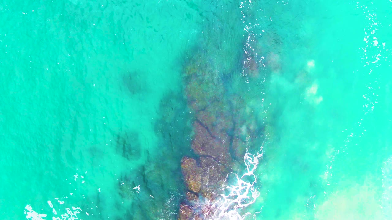 Overhead view of clear turquoise water at Punta Buzzards, Baja California Sur, with submerged rocks low in frame and no visible people.