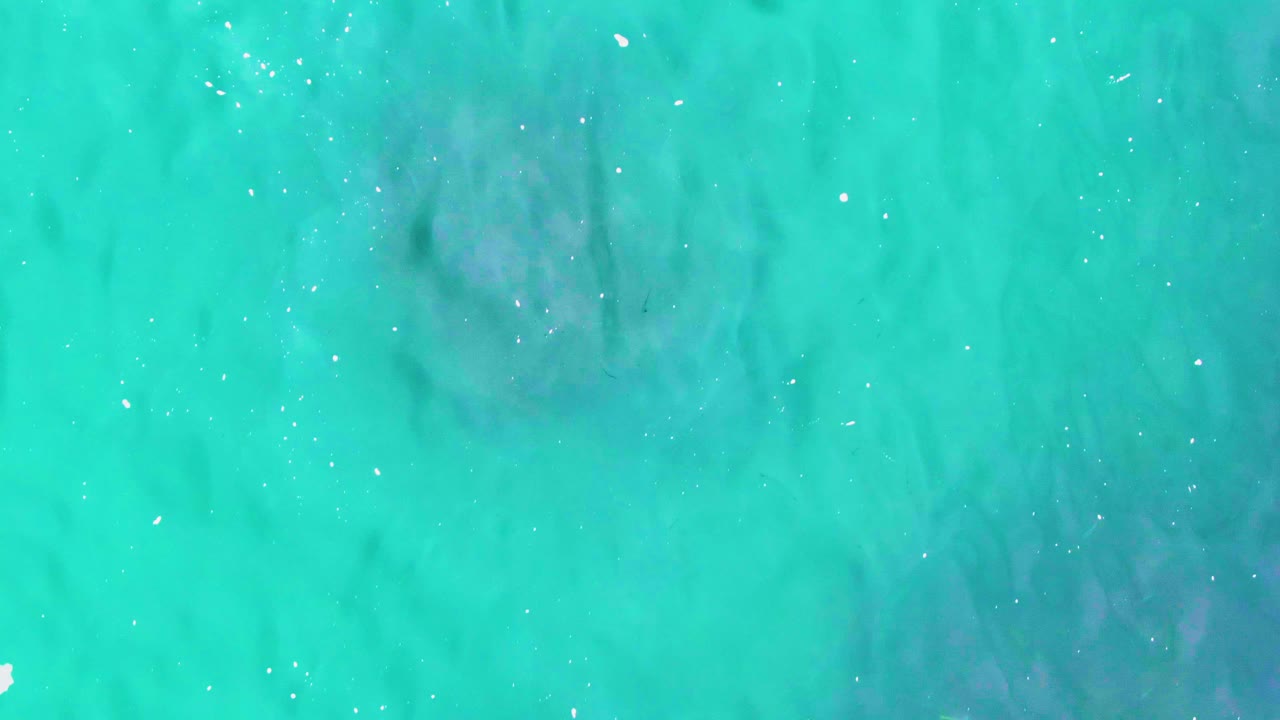 Turquoise ocean water with faint dark underwater clouding and white surface specks.