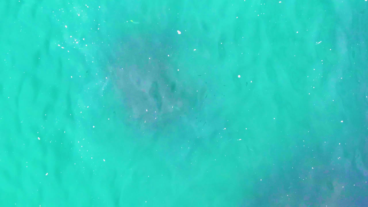 Turquoise ocean water at Punta Buzzards with a darker submerged patch more apparent near the upper center, small white flecks on the surface, and no visible people.