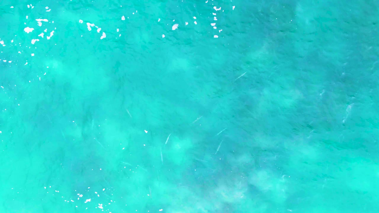 Turquoise water with foam specks and visible shallow seabed texture.