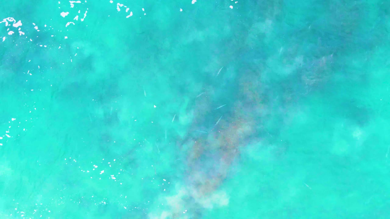Straight-down Buzzards Beach water view with bright turquoise color, small white foam marks near the upper edge, pale underwater clouding, and no visible people.