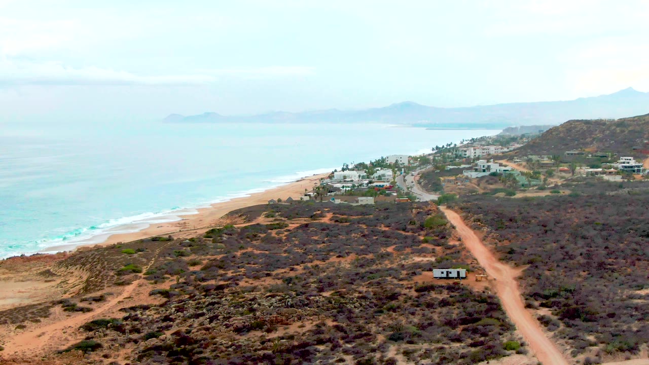 Coastal dirt road running past scrub toward beach houses
