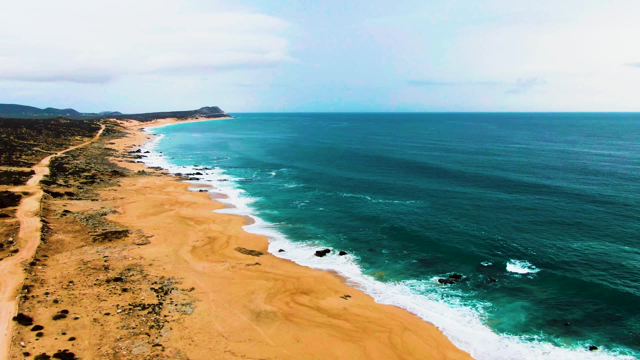 Aerial coastline with dirt track, beach, and ocean