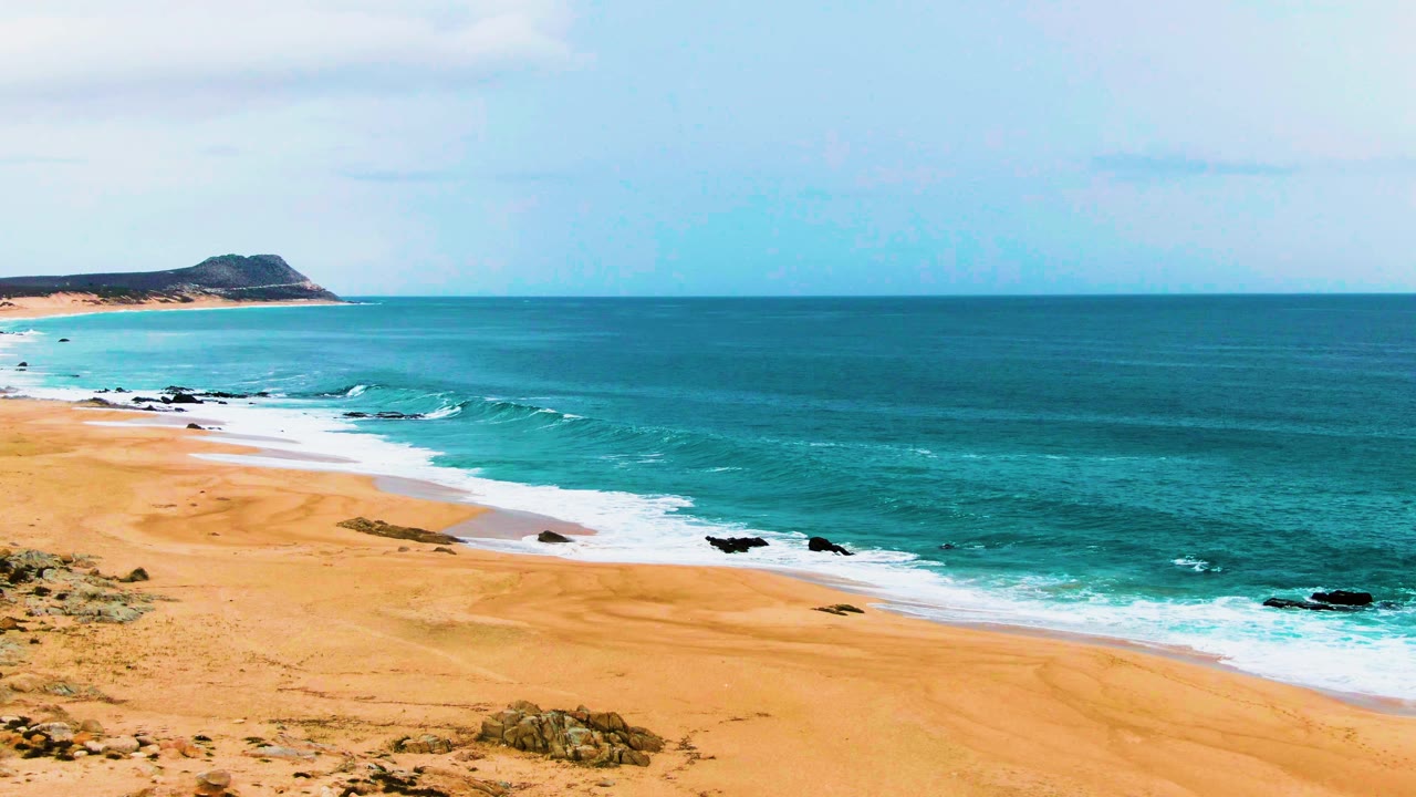 Wide beach with turquoise surf, golden sand, rocks, and distant headland