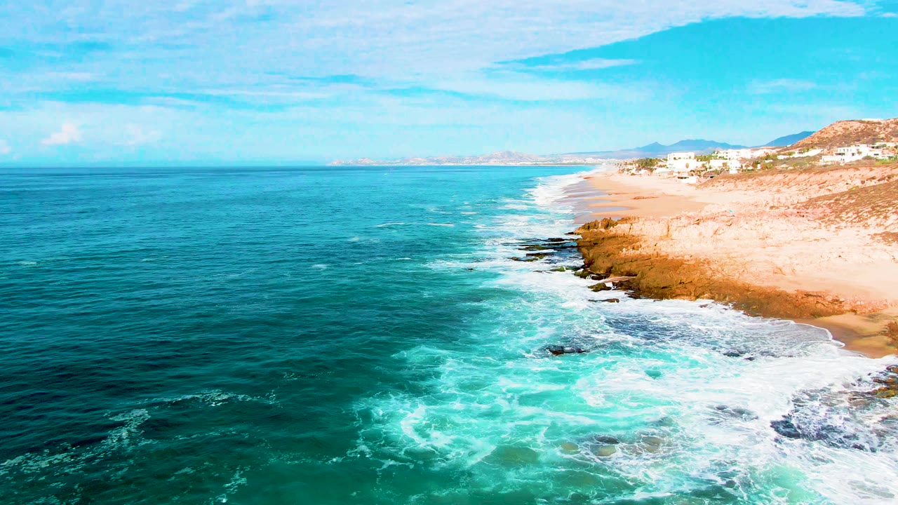 Wide aerial shoreline with deep blue ocean and white foam along rocks.