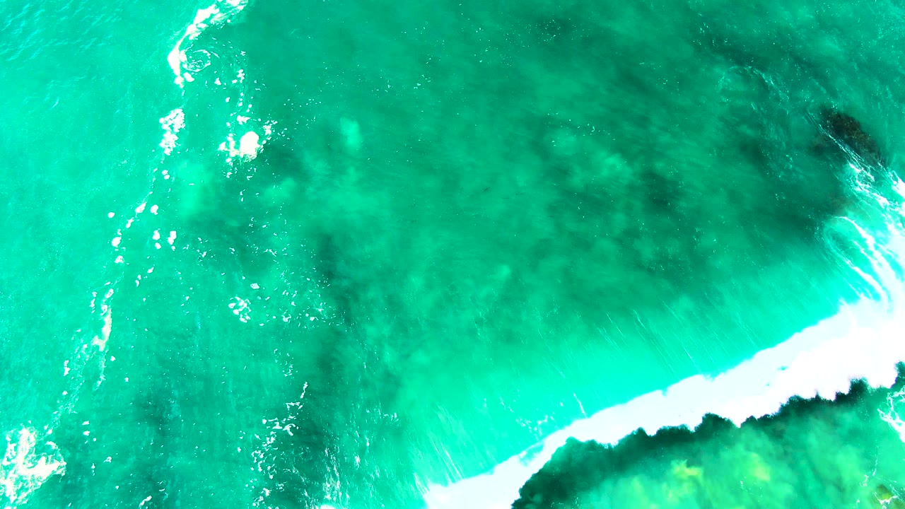 At 0:01, the Punta Buzzards aerial view shows a bright foam line cutting across turquoise water above darker submerged reef forms, with no visible people.