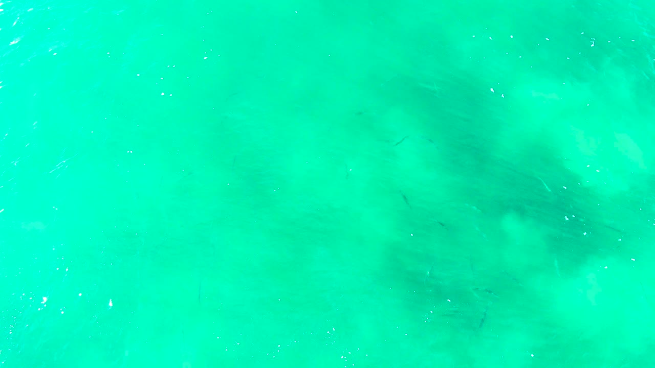 Clear turquoise ocean water at Punta Buzzards, Baja California Sur, with faint darker seabed patches beneath soft surface ripples and no visible people.