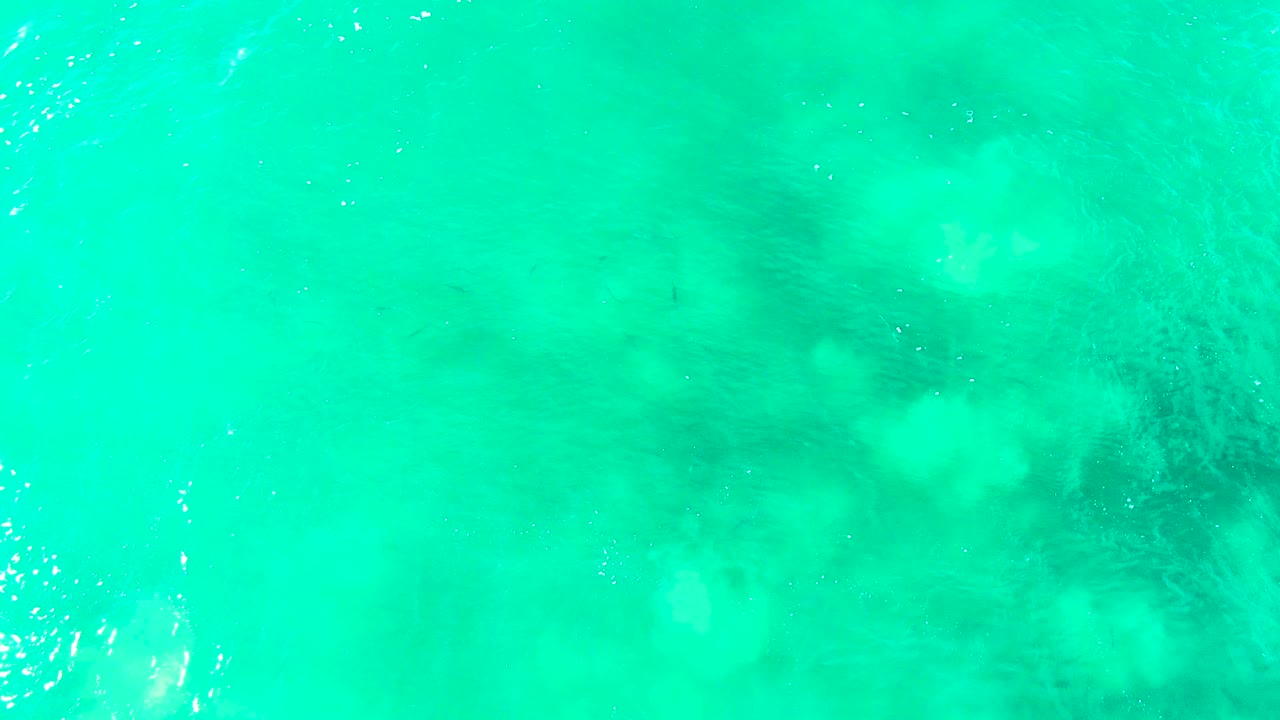 Turquoise water with faint foam along the left edge and darker underwater features.