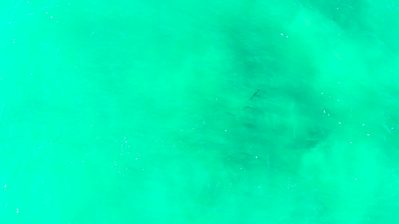 Overhead view of turquoise ocean water at Punta Buzzards, Baja California Sur, with faint darker underwater patches and no visible people.