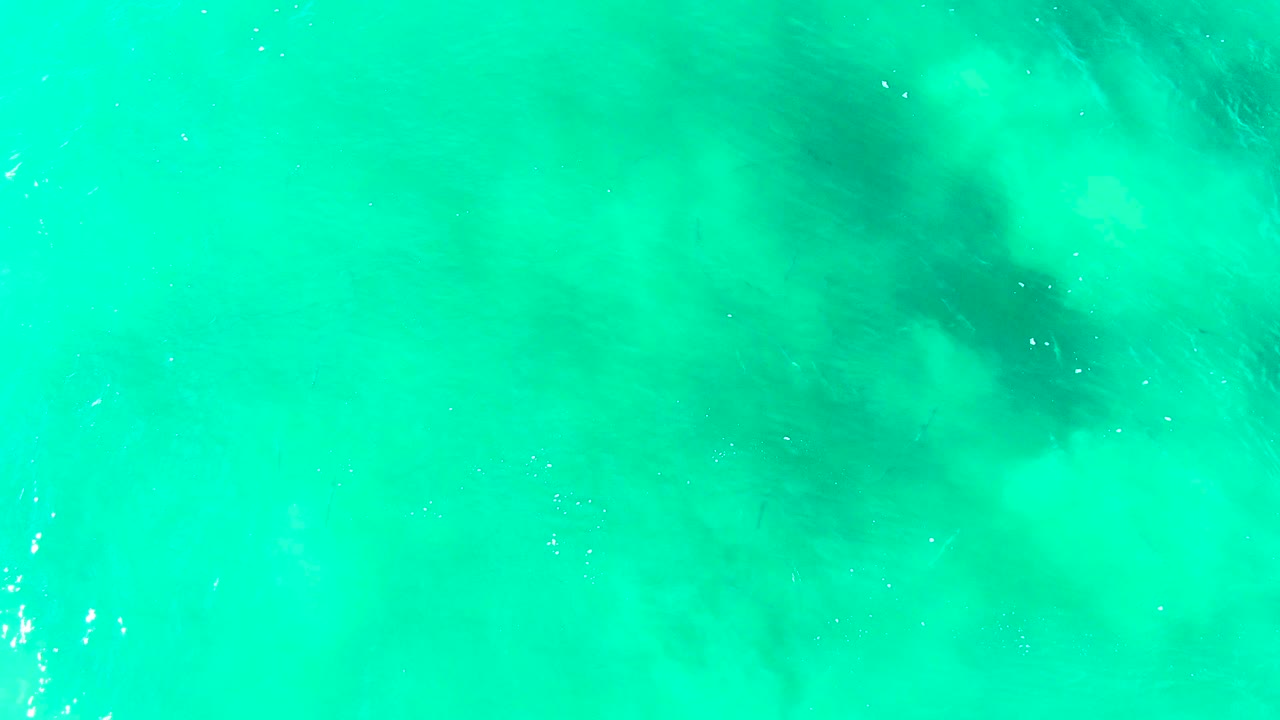 Overhead view of turquoise shallow water at Punta Buzzards, Baja California Sur, with muted darker seabed patches beneath the surface and no visible people.