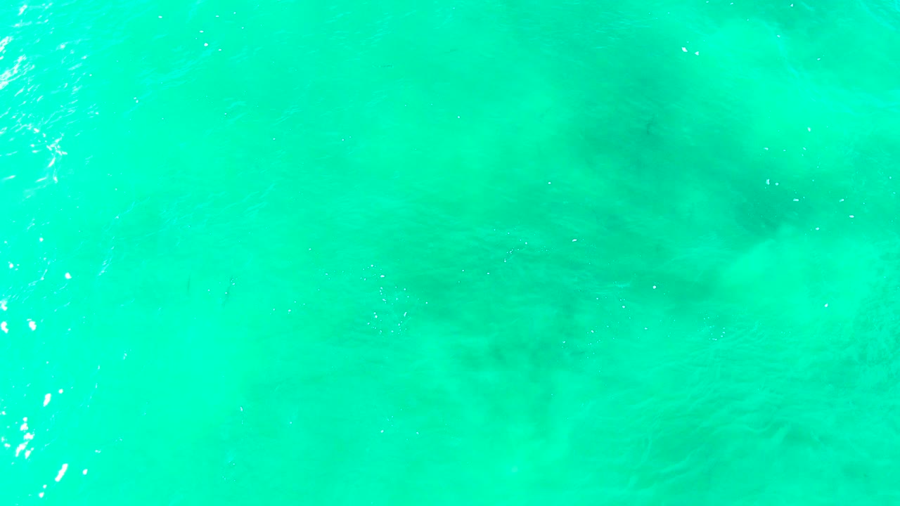 Shallow turquoise sea with darker seabed pattern near center.
