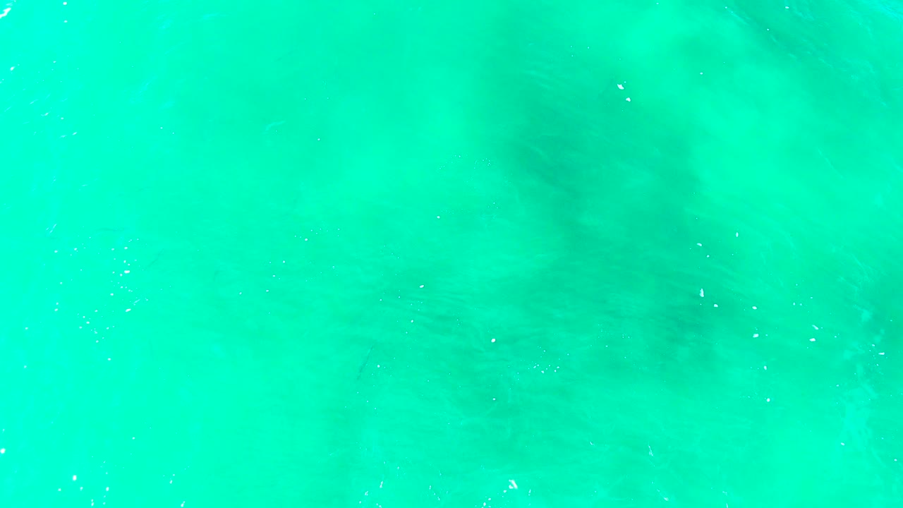 Top-down view of turquoise shallow ocean water at Punta Buzzards, Baja California Sur, with subtle underwater floor patterns and no visible people.