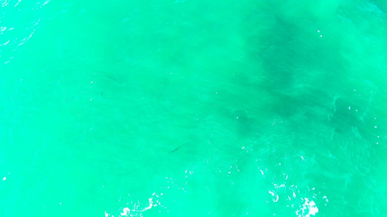 Turquoise ocean water at Punta Buzzards fills the first frame with small ripples, faint darker underwater areas, and no visible people.