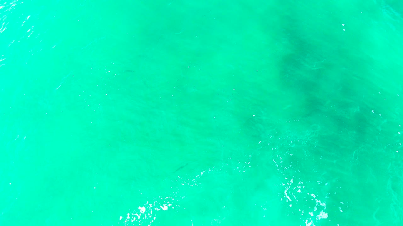Turquoise ocean surface with subtle ripples and foam near the lower edge.