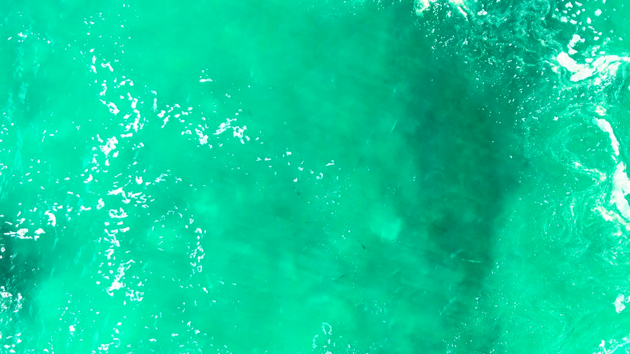 Overhead turquoise ocean water at Punta Buzzards, Baja California Sur, with bright surface foam along the left side, a darker submerged patch near center, and no visible people.