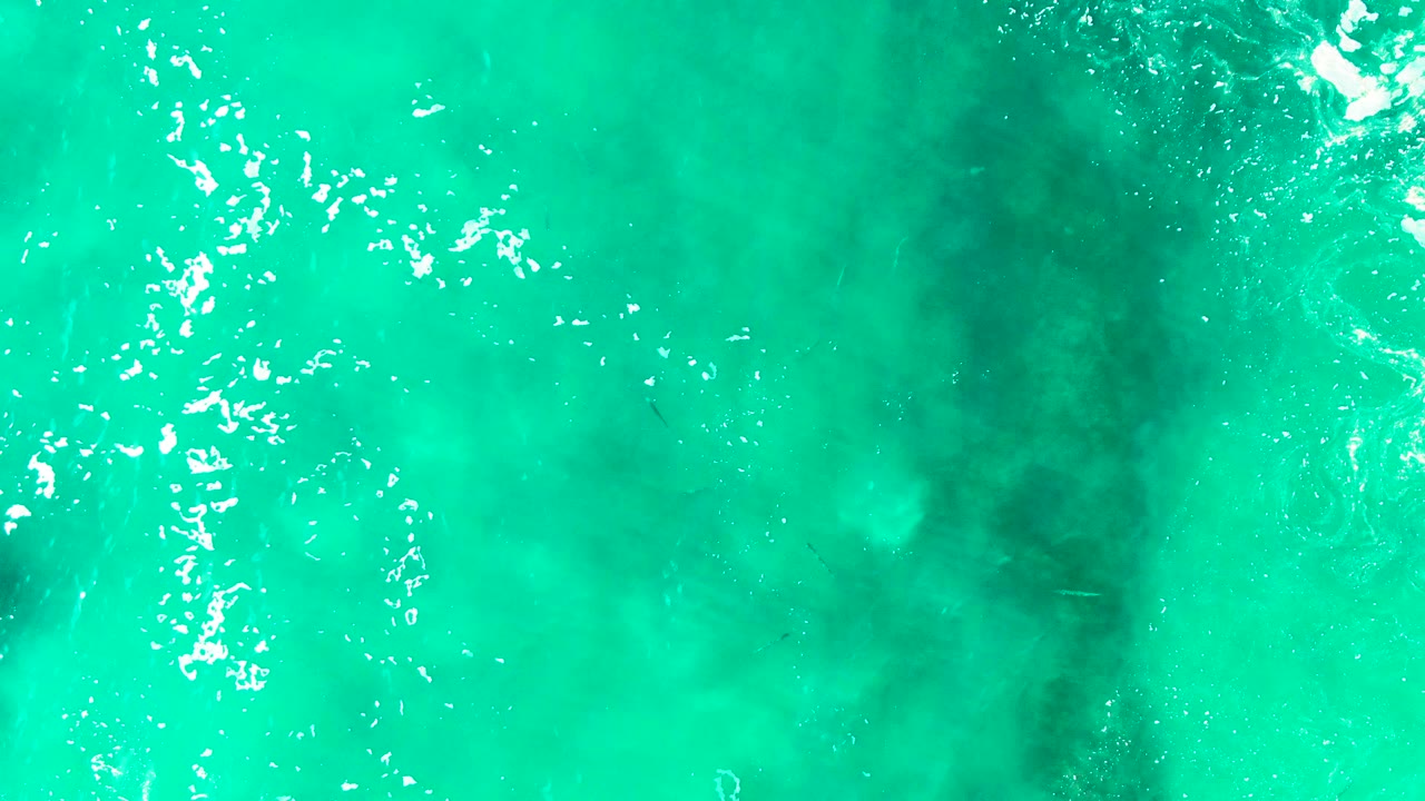 Aerial-looking frame of Punta Buzzards turquoise ocean water with a darker patch slightly right of center, foamy highlights near the upper left, and no visible people.