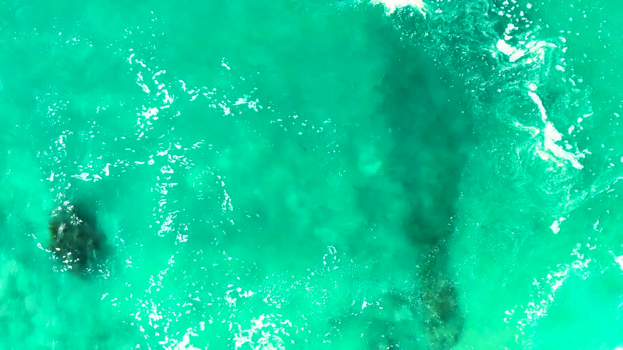 Turquoise ocean water over dark submerged rock formations.