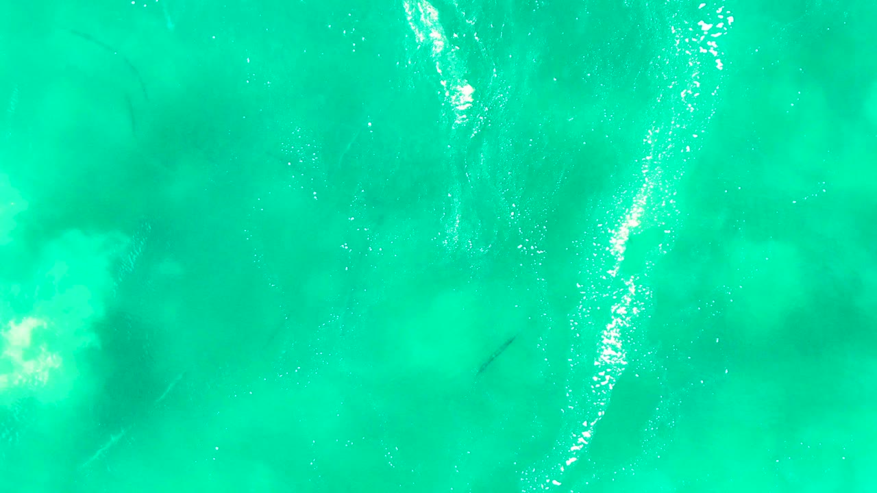 Clear turquoise ocean water at Punta Buzzards, Baja California Sur, with scattered white foam and a faint fish shadow lower in the frame, no visible people.
