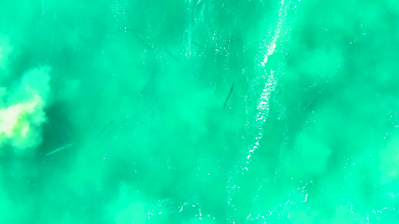 Turquoise sea surface with cloudy pale wash and underwater shapes.