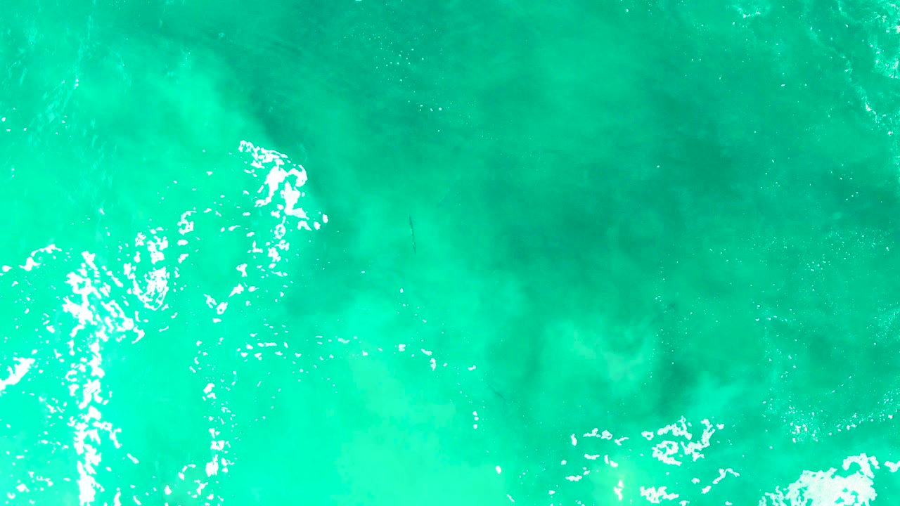 Aerial view of turquoise water in Baja California Sur with white breaking foam spread across the middle of the frame and no visible people.
