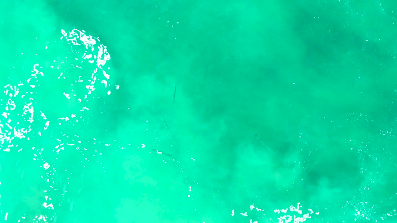 Top-down view of turquoise ocean at Punta Buzzards with scattered white foam along the left side and no visible people.