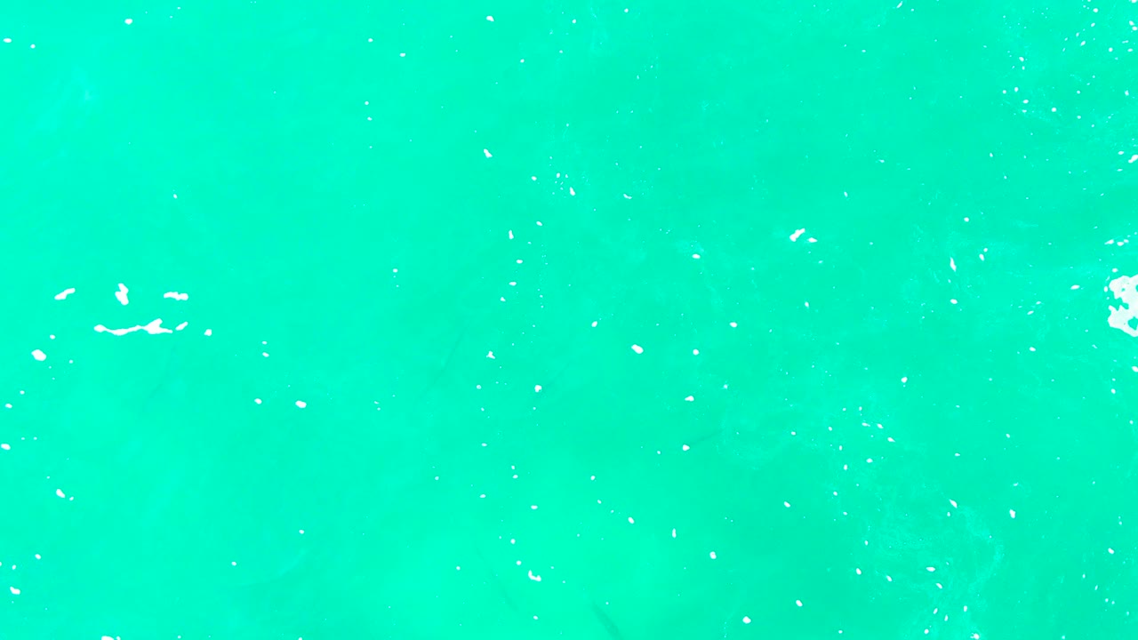 Overhead view of turquoise ocean water at Punta Buzzards with scattered white foam flecks and no visible people.
