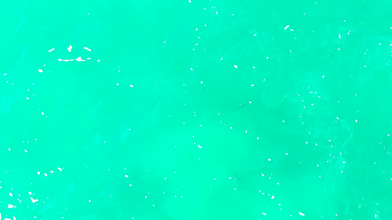 Overhead Punta Buzzards water view with brighter turquoise tones, small foam clusters, and faint darker areas under the surface, with no visible people.