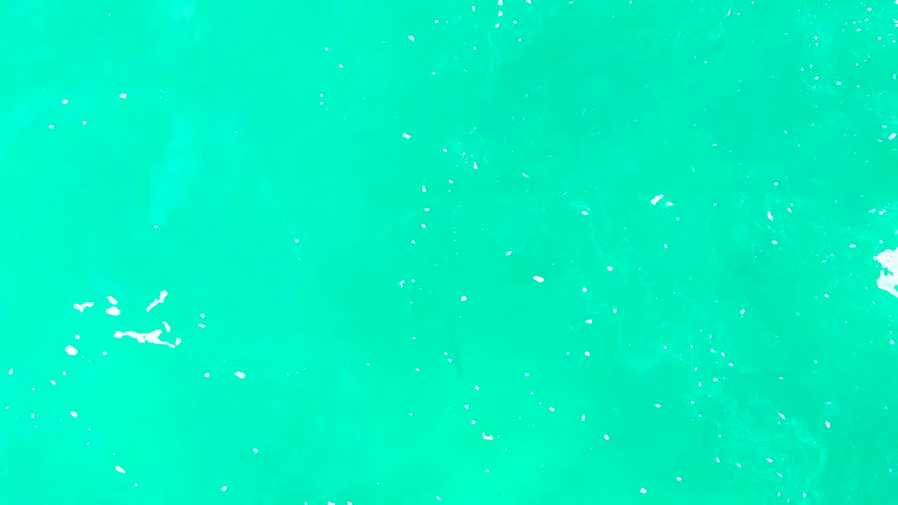 Overhead view of turquoise ocean at Punta Buzzards, Baja California Sur, with small white foam patches near the upper left and no visible people.