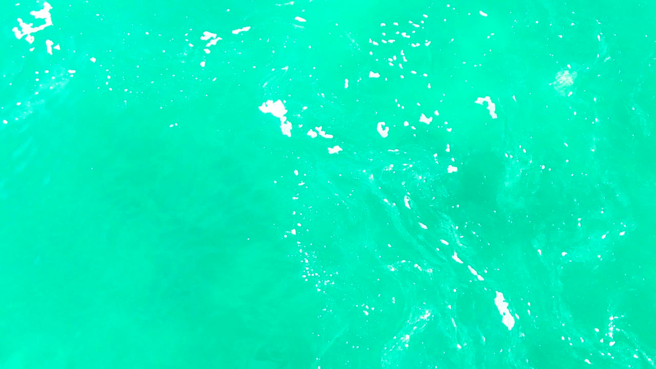 Open turquoise water at Punta Buzzards with foam streaks near the left edge and soft underwater color variation, with no visible people.