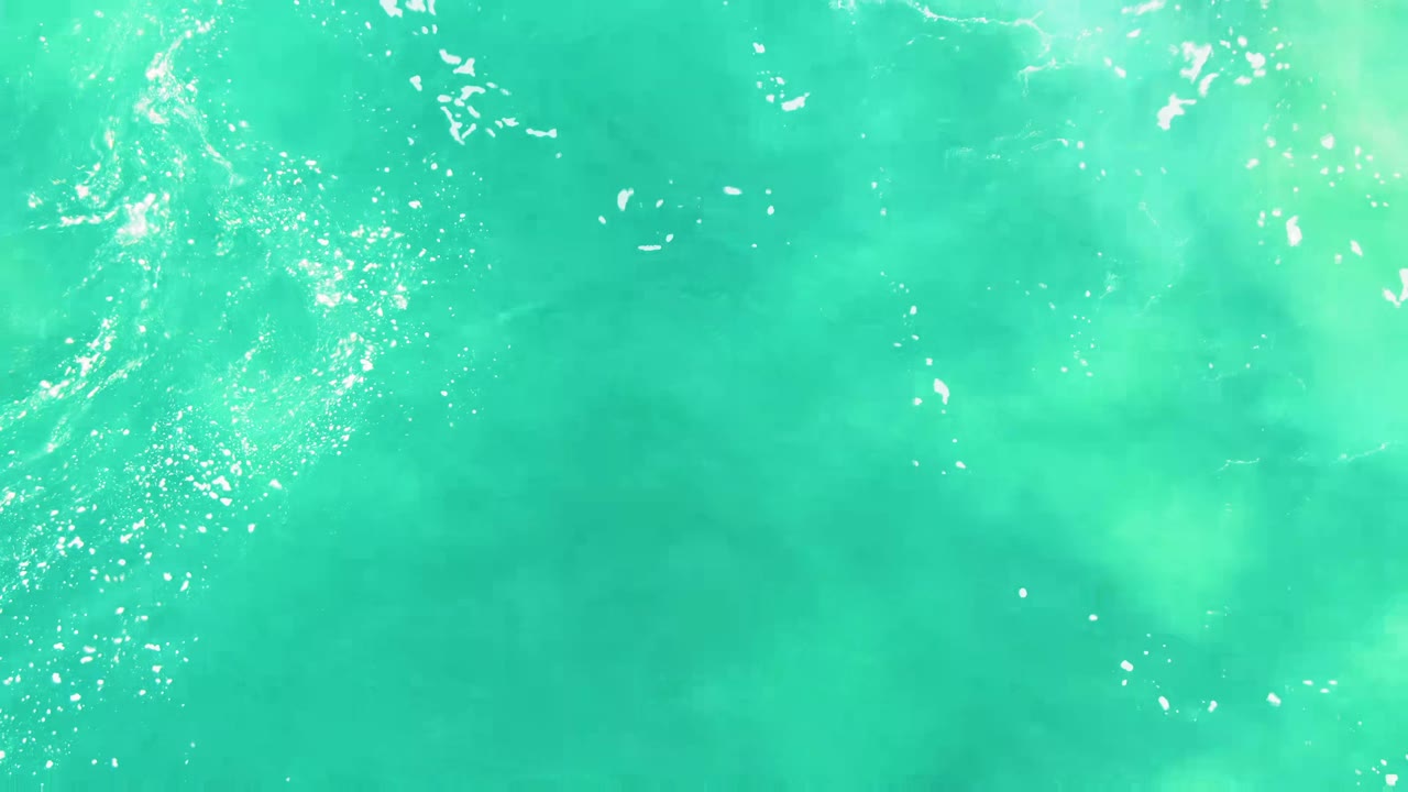 Overhead turquoise ocean water at Punta Buzzards, Baja California Sur, with scattered white foam flecks near the left side and no visible people.