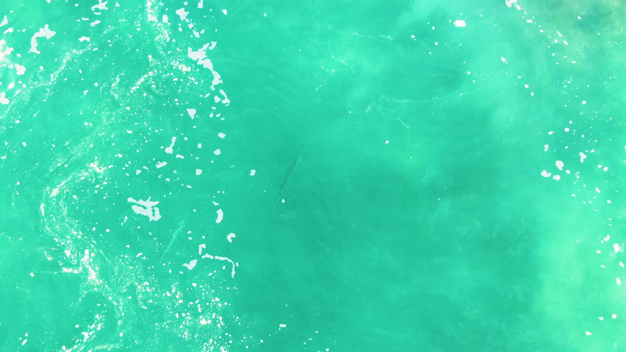 Top-down view of turquoise ocean water at Punta Buzzards, Baja California Sur, with white foam clustered along the left side and no visible people.