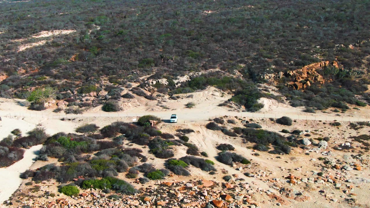 White car on sandy desert road with rocky foreground