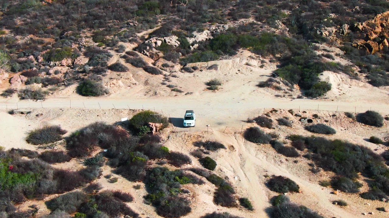 White car farther along a pale road through dry brush.