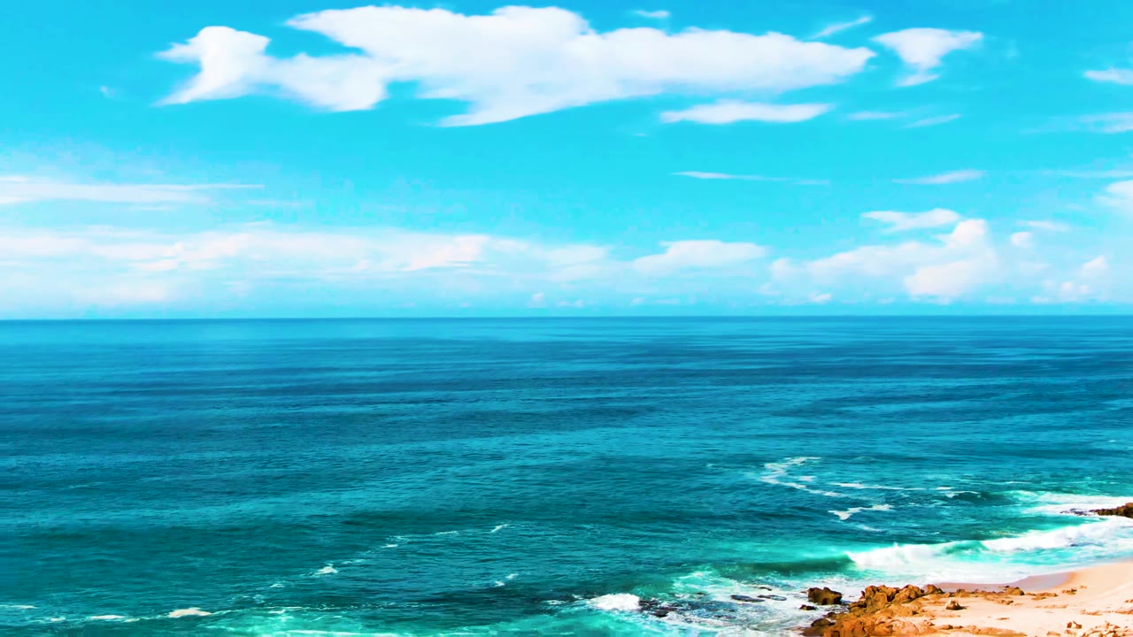 Punta Buzzards coastline in Baja California Sur with deep blue water, turquoise shallows, white surf near rocks and sand, scattered clouds, and no visible people.