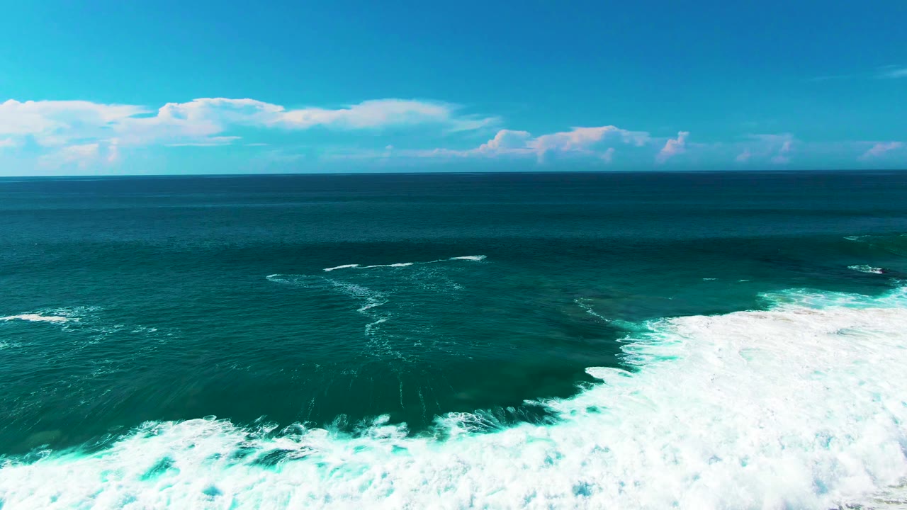 Aerial view of turquoise ocean at Punta Buzzards, Baja California Sur, with broad white surf foam entering from the lower right and no visible people.