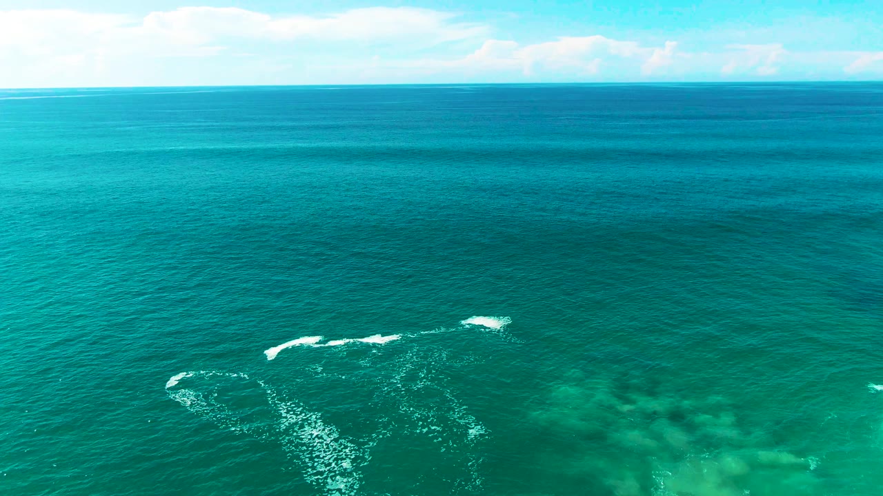 Aerial view of turquoise sea with white wave breaks and no shoreline.