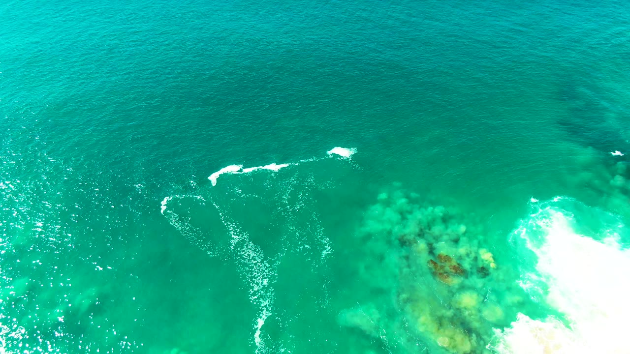Overhead ocean surface with curved foam trail and visible seabed patches.