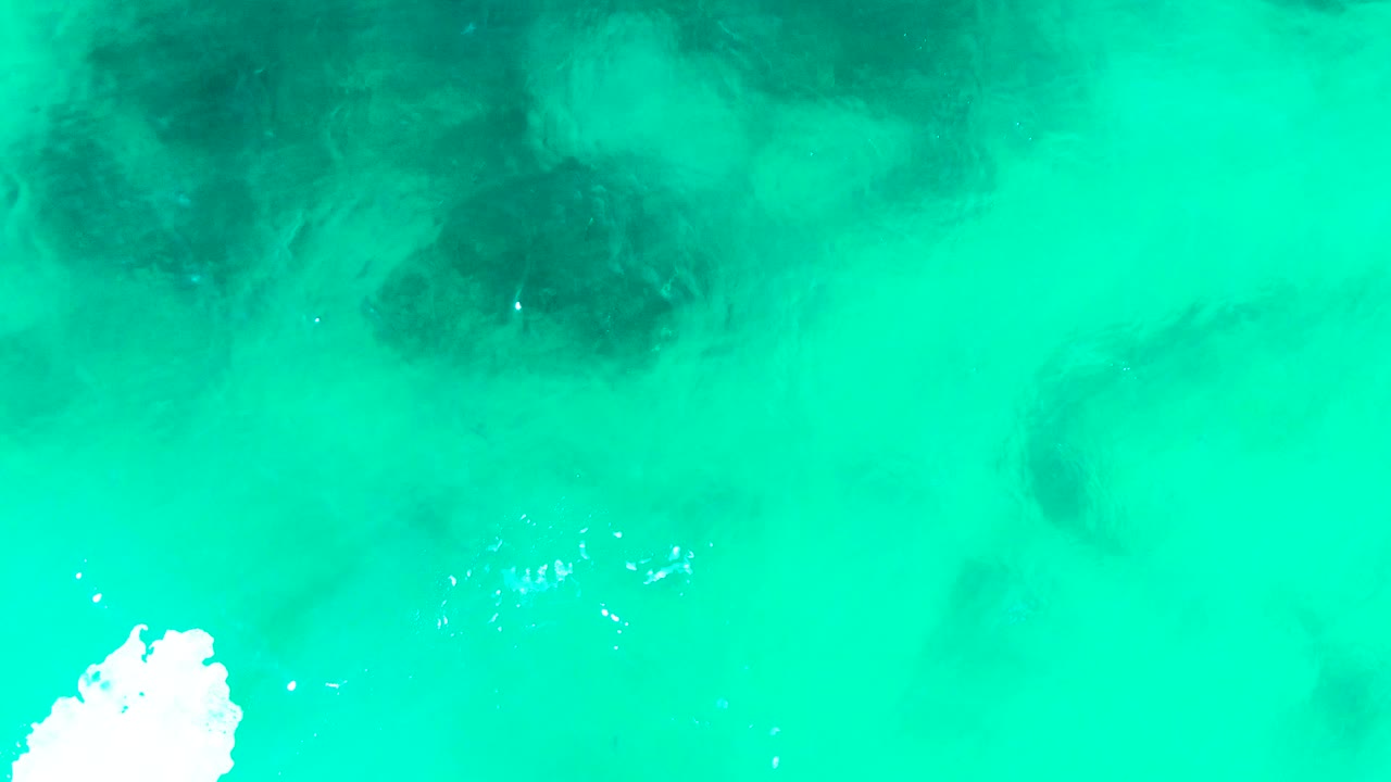 Turquoise water and shadowy underwater formations with foam along the lower left edge.