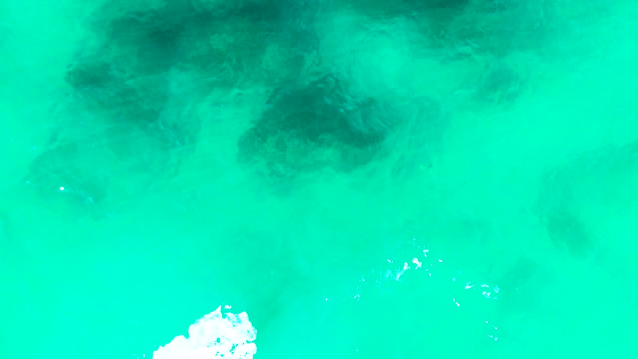 Turquoise ocean water with dark underwater patches and white foam near the lower edge.