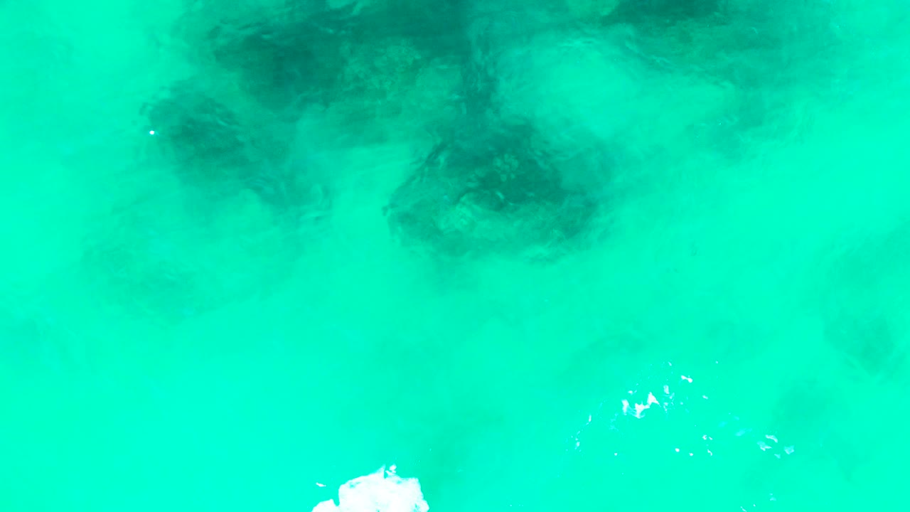 Overhead Punta Buzzards frame with turquoise water filling the view, soft dark underwater shapes across the upper area, scattered white surface highlights, and no visible people.