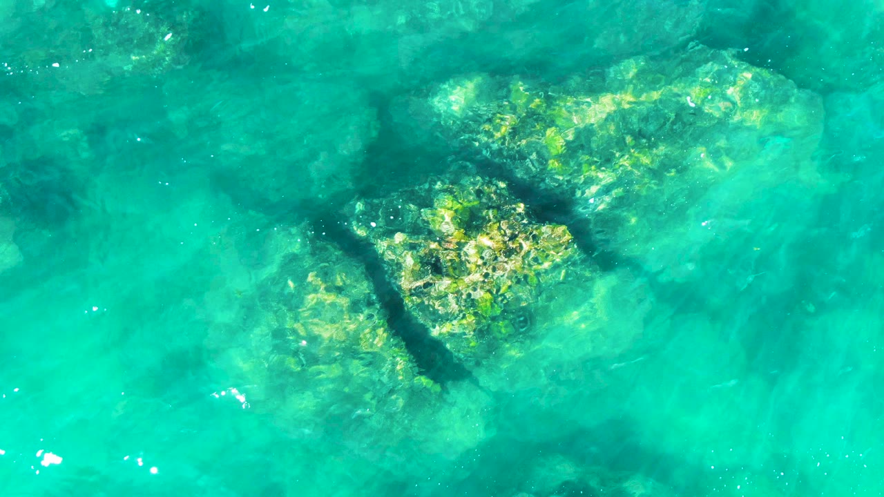 At 0:01, the overhead view at Buzzards Beach shows the turtle shape under green-blue water beside bright submerged rocks, with no visible people.