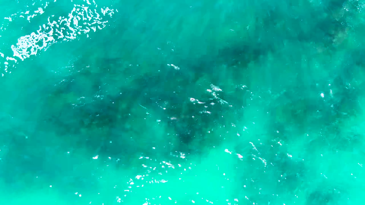 Turquoise ocean water with darker underwater rocks and white ripples.