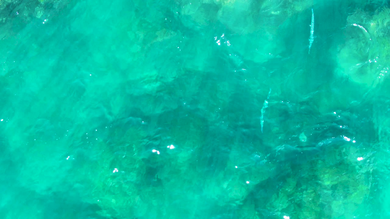 Bright turquoise water with darker underwater rock shapes.