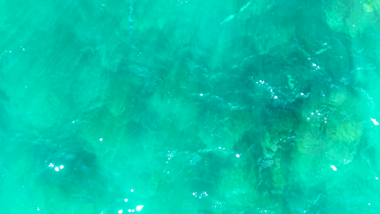 Rippling turquoise ocean with submerged rock formations.