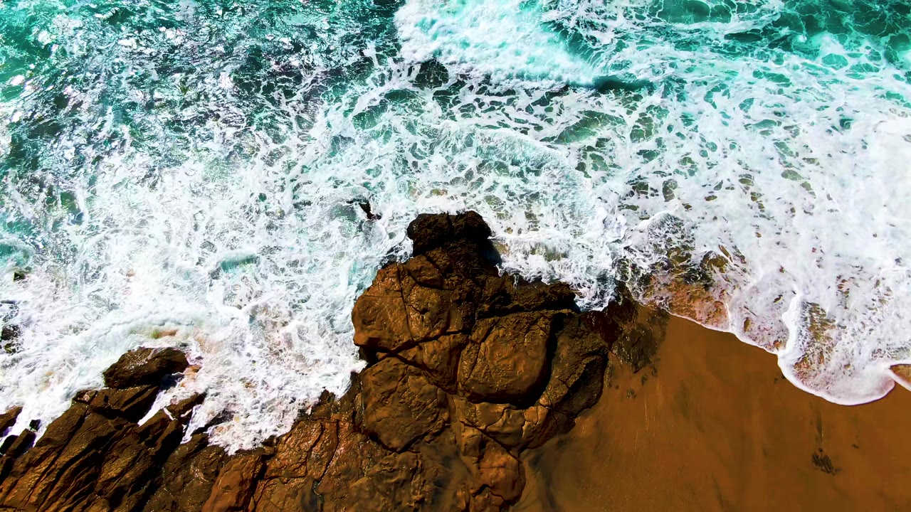 At Buzzards Beach in Baja California Sur, foamy water covers much of the rocks while a curved wash line reaches across the sand, with no visible people.