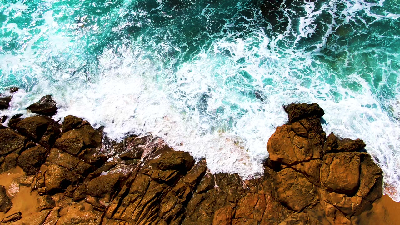 At 0:01, white foam pushes farther over the rocky Punta Buzzards shoreline while turquoise water fills the upper frame and no visible people appear.